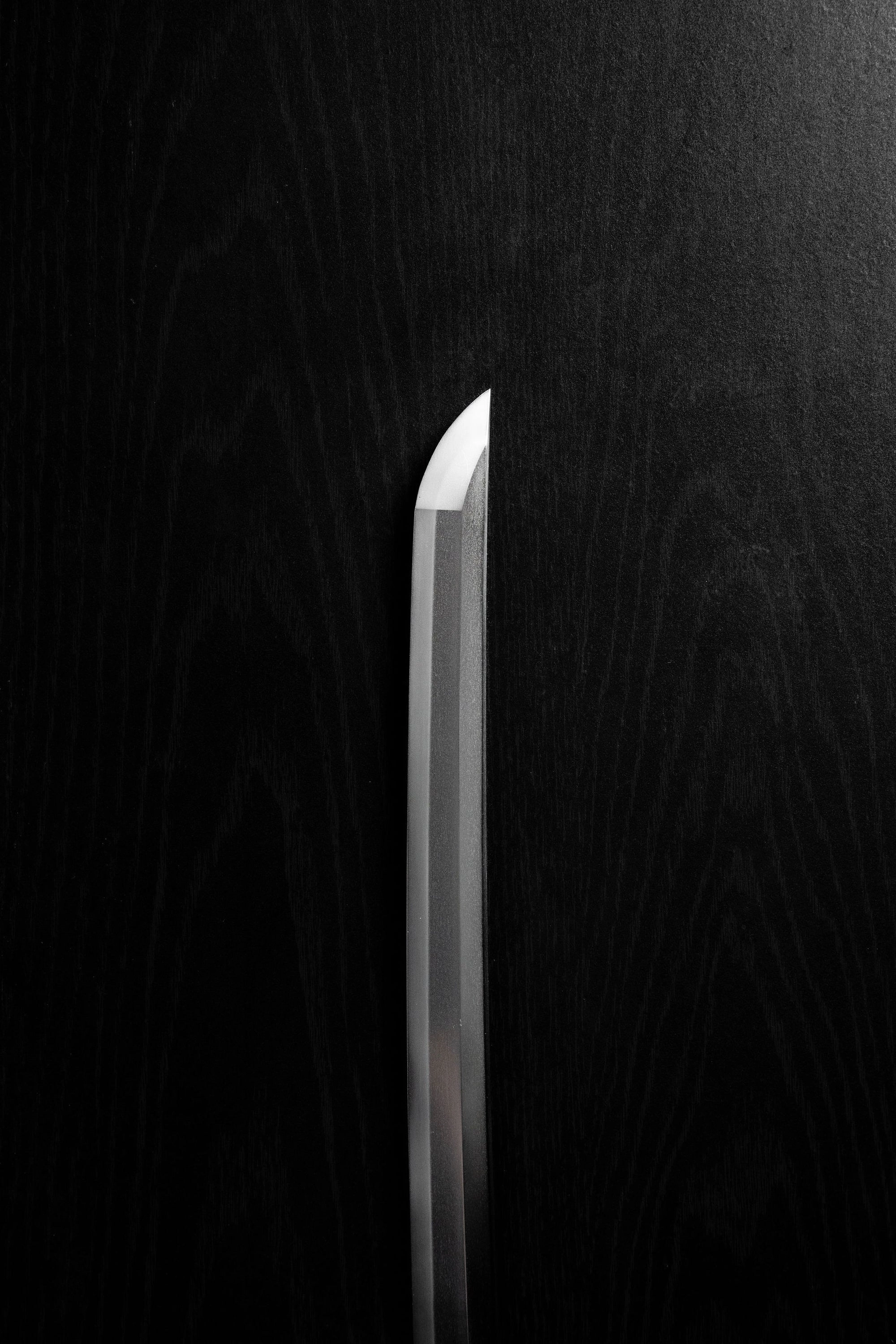 The tip of a katana blade standing upright against black